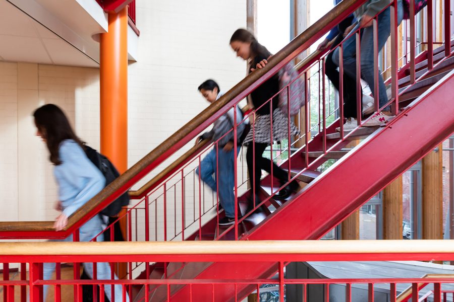 Leerlingen van College de Heemlanden die naar beneden lopen van een rode trap af in het schoolgebouw