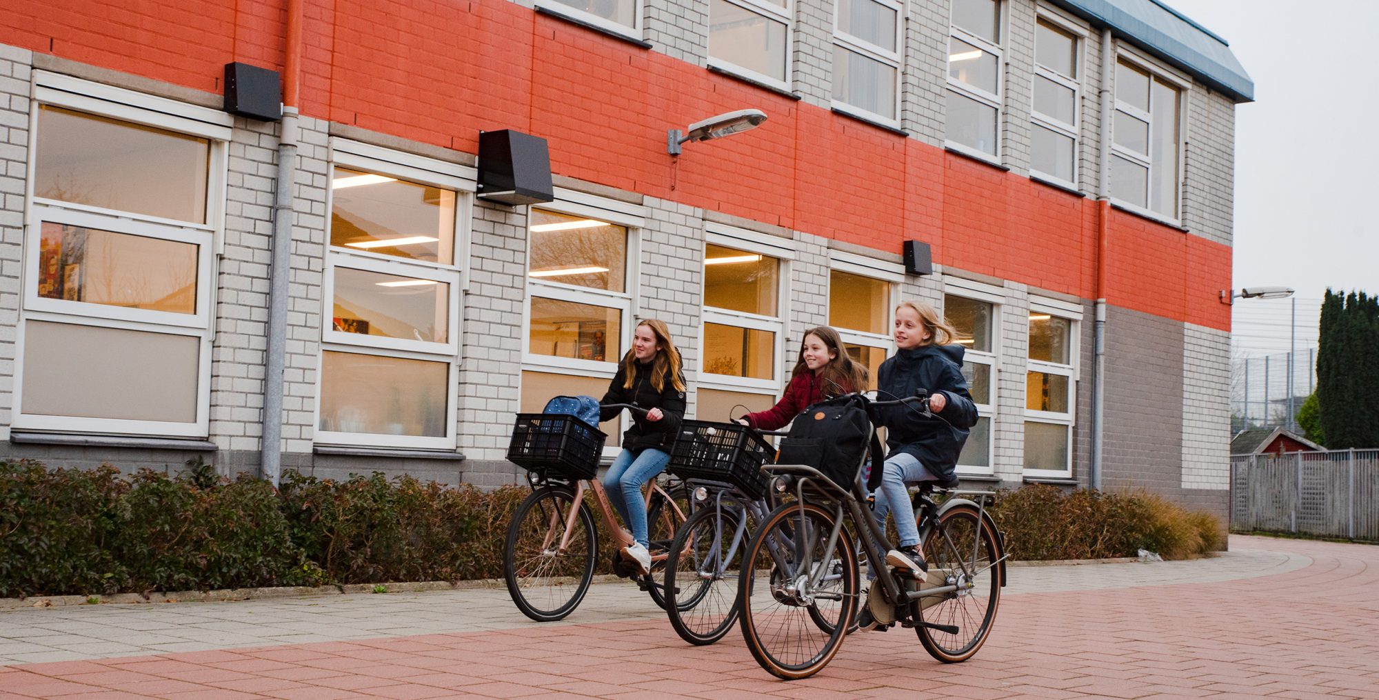 Drie meisjes leerlingen van College de Heemlanden ieder op een fiets, fietsen voor de school